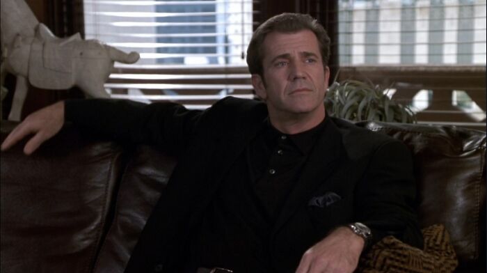 Man in a black suit sitting on a couch with a pensive expression, representing poor portrayal of women in films.