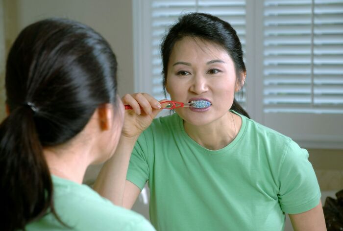 Person brushing teeth in front of a mirror, practicing good hygiene habits.