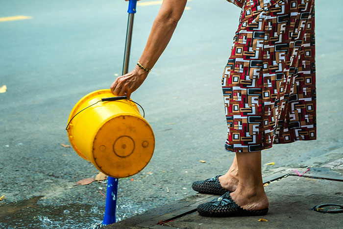 Person handling yellow bucket of water on street in cold weather, neighbor causing disruption.