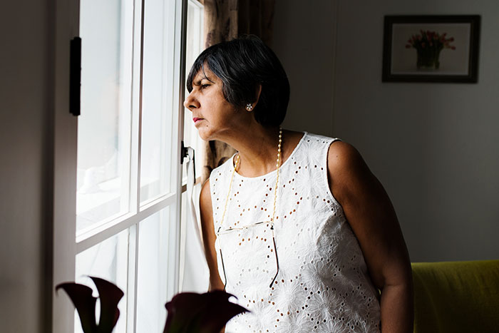 Woman in a white dress looking out the window, contemplating the neighbor's havoc with water in freezing temperatures.