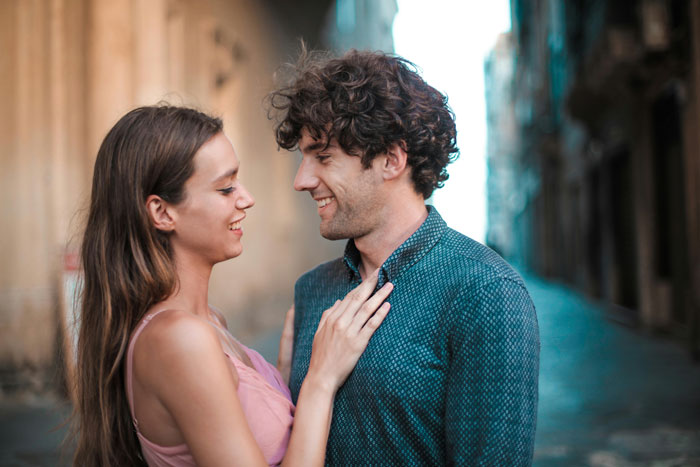 A couple smiling at each other in an alley, illustrating relationship dynamics in a neighbourhood affair context.