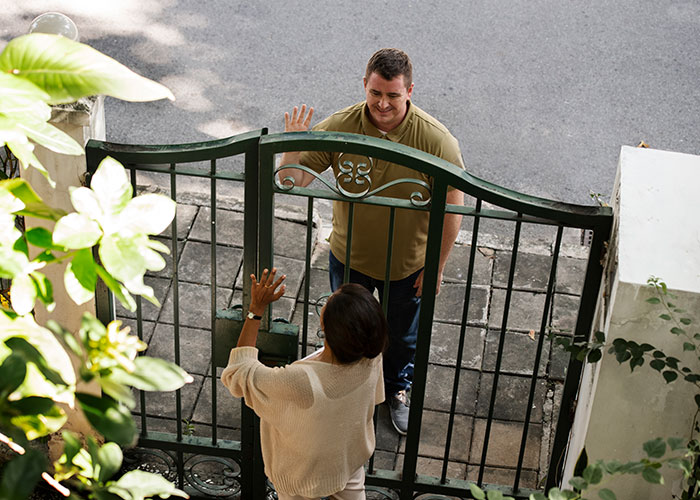 Couple in town greeting neighbor through gate, expecting a warm welcome.