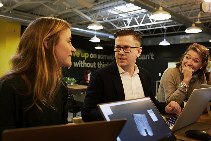 Three people discussing work on laptops in a modern office, highlighting changes in obvious knowledge over the years.