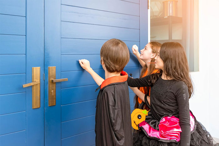 Children in costumes knocking on a blue door, representing old Halloween traditions.