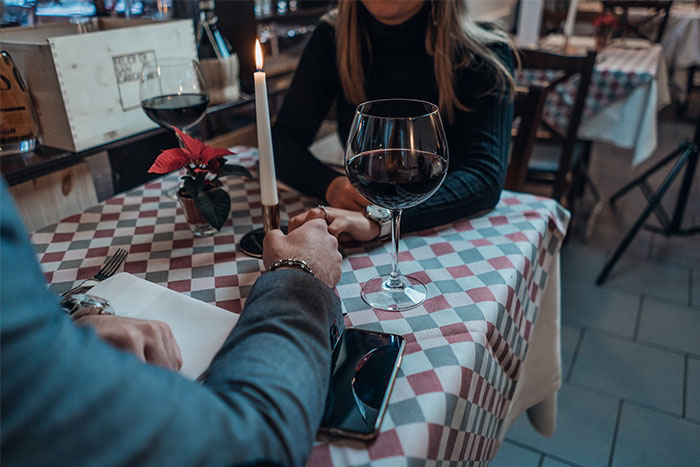 Couple holding hands across a restaurant table set with wine and a candle, symbolizing changing relationship norms over time.