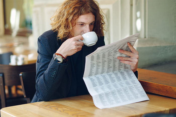 A person reading a newspaper while drinking coffee, symbolizing things that used to be obvious but are now confusing.