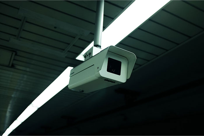 A ceiling-mounted surveillance camera inside a dimly lit building, representing technology changes over the years.