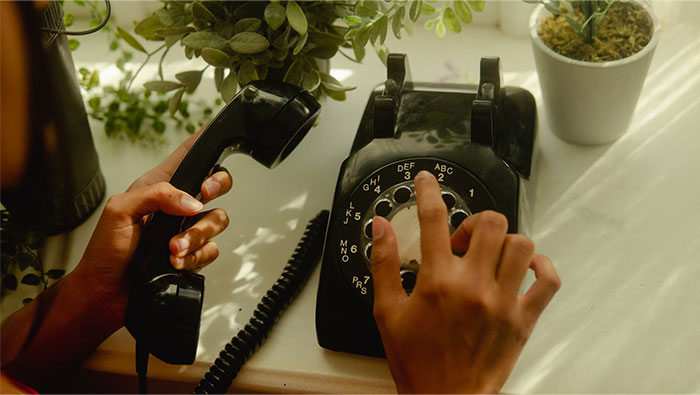 Person dialing a rotary phone, a once obvious object, now confusing to many.