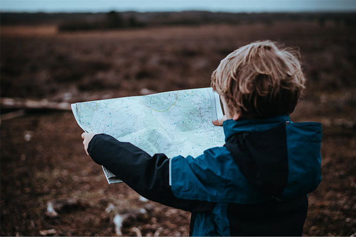 Child in blue jacket holding a map outdoors, symbolizing once obvious navigation skills now confusing for many.