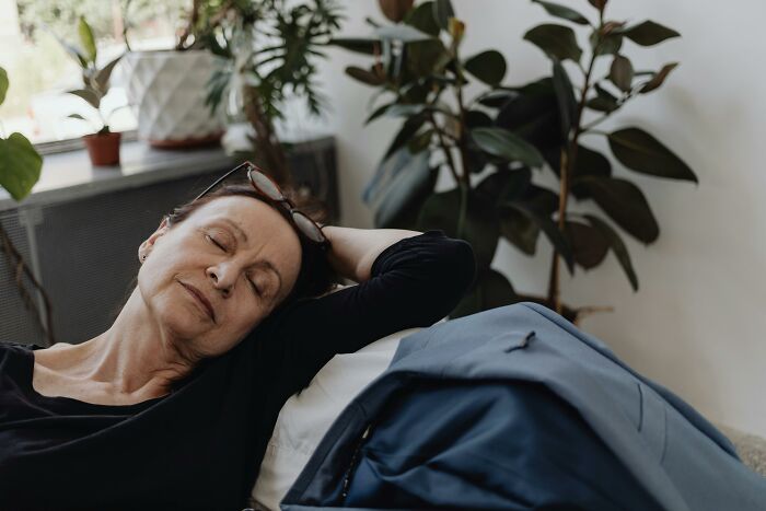 Older parent relaxing on a couch in a cozy room with plants in the background.