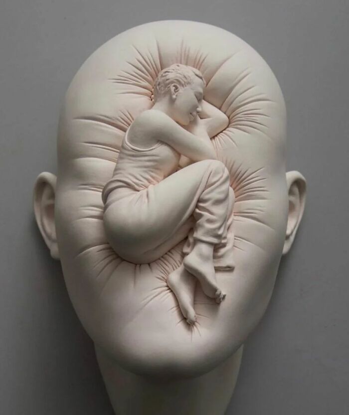 Realism and surrealism blend in a sculpture of a figure curled up within a textured head.