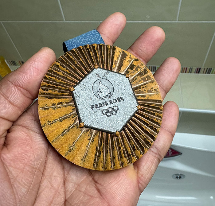 Hand holding a rusted bronze medal with Paris 2024 Olympics logo, highlighting French Olympians.