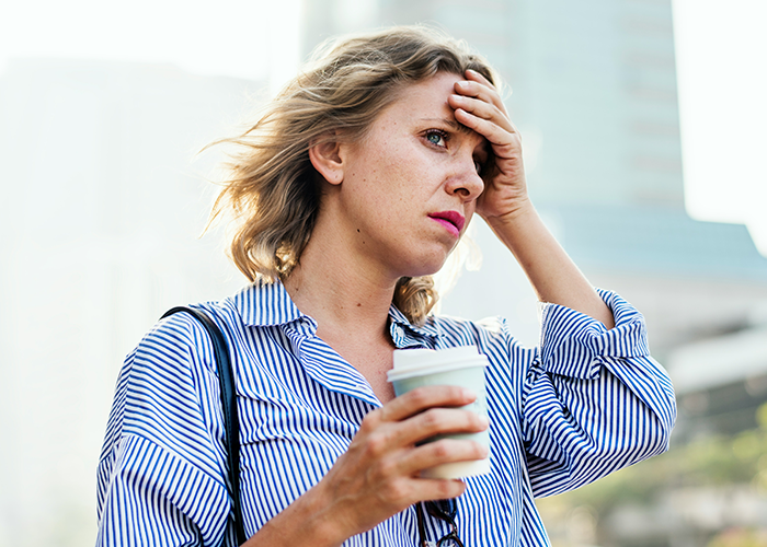 A frustrated woman holds a coffee cup, standing outdoors, learning a lesson about parking in driveways.