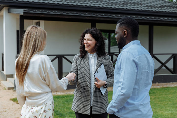 Two partners with a third person, standing outside a house.