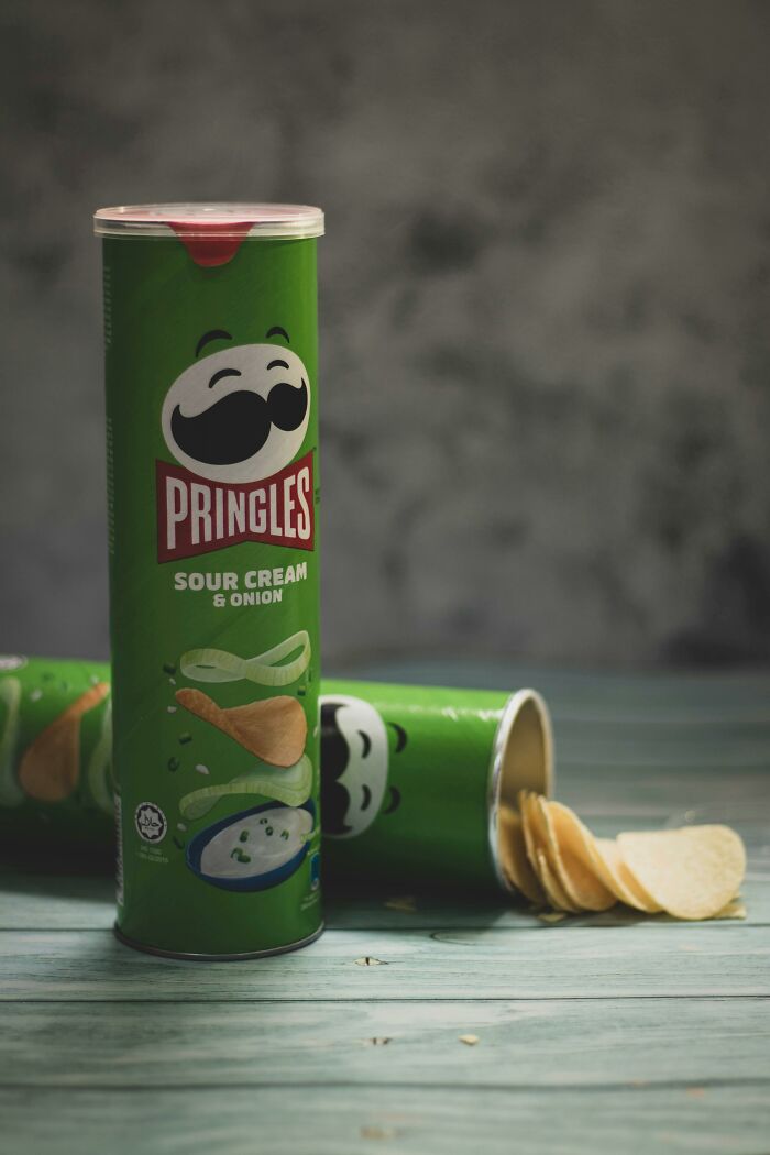 Green sour cream and onion Pringles can stand upright on a table with an open canister beside it.