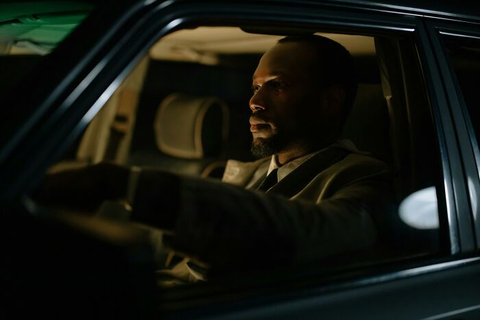 Man seated in a dimly lit car, showcasing survival against all odds.