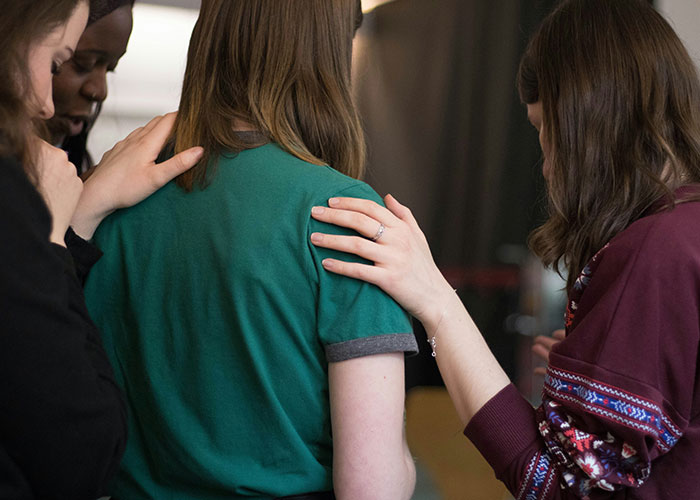 A group supports each other, hands resting on shoulders, illustrating persistent Mormons bonding in a spiritual setting.