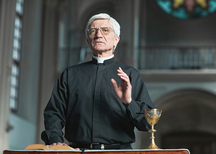 A person in clerical attire stands in a church near a chalice, illustrating persistent Mormons learning a lesson.