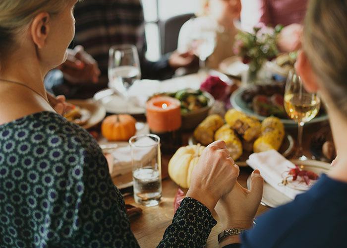 People gathered around a dinner table, holding hands in a moment of gratitude, with a variety of food and candles.