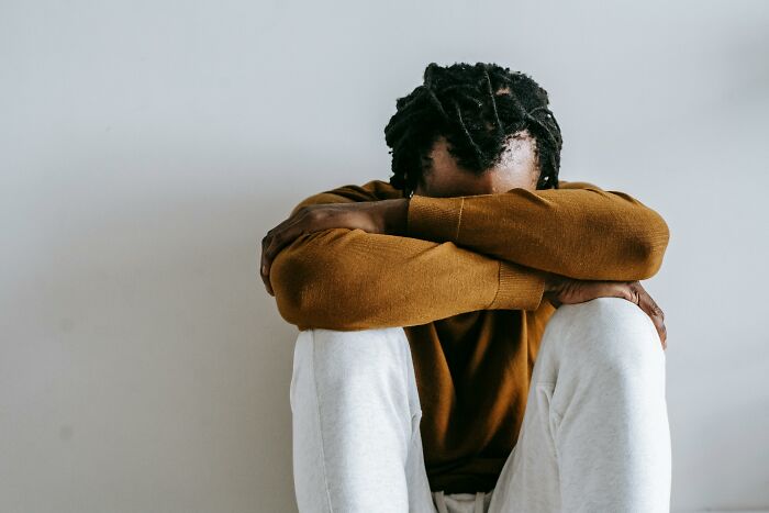 Person in brown sweater and white pants sitting with arms on knees, evoking emotional intensity, related to "You Up?" text moments.