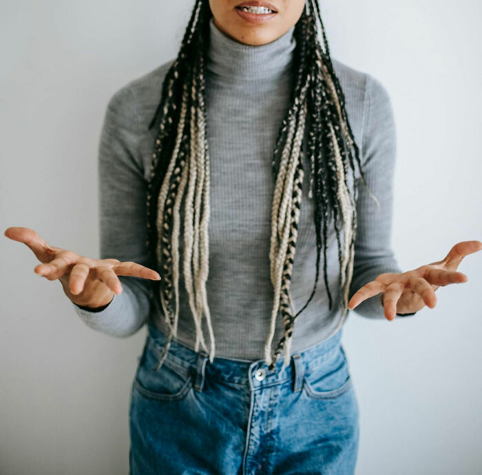 Person in gray turtleneck with braided hair, gesturing with both hands, capturing a moment realized dating idiot.