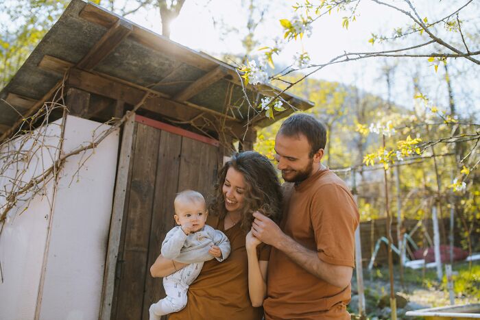 A family shares a moment outdoors, smiling and holding a baby, surrounded by nature, embodying knowing secrets of joy.