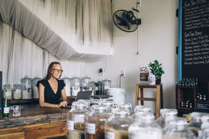 Person working on a laptop in a shop, surrounded by jars and shelves, representing sudden job loss.