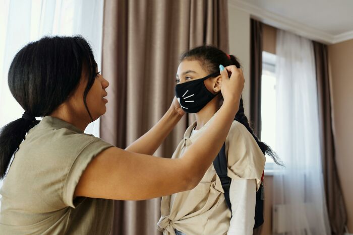 Woman helps child adjust a mask with a whisker design.