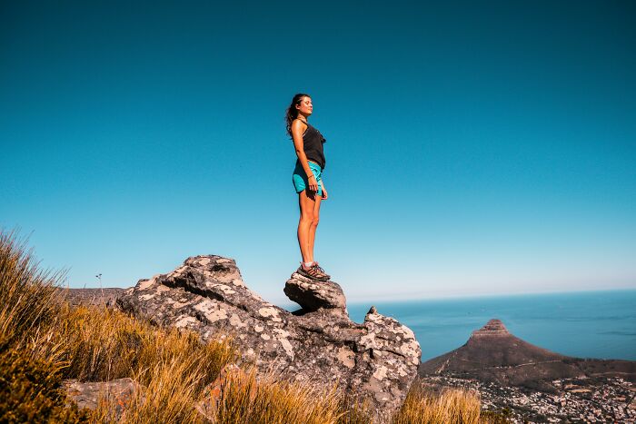 Woman standing confidently on a rock with a scenic mountain view, highlighting WomenInMaleFields empowerment.