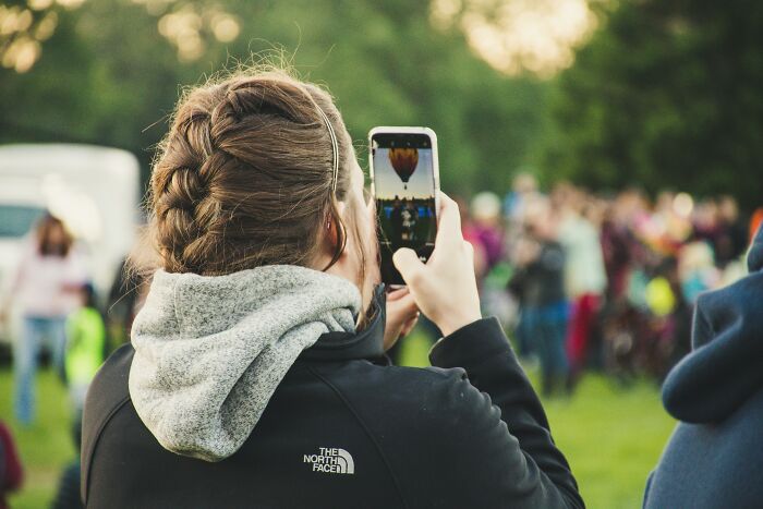 Person taking a photo with a smartphone at an outdoor event, subtle judgment in people's expressions around.