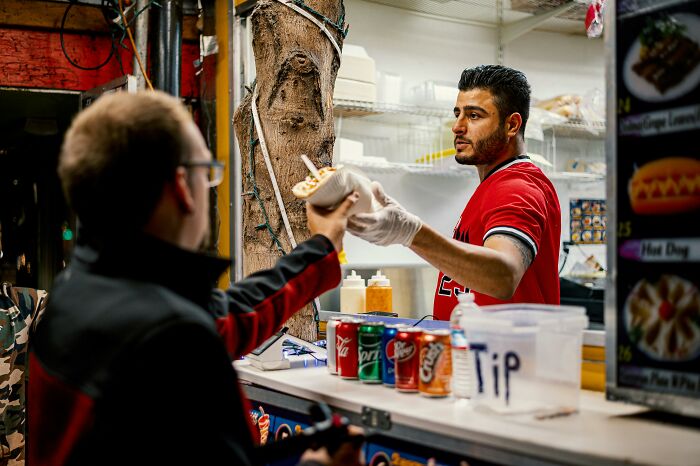 A vendor in a red shirt serves food to a customer at a street food stand, representing challenging job experiences.