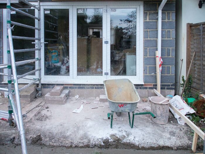 Construction site with a wheelbarrow, scaffolding, and unfinished building materials, representing challenging work conditions.