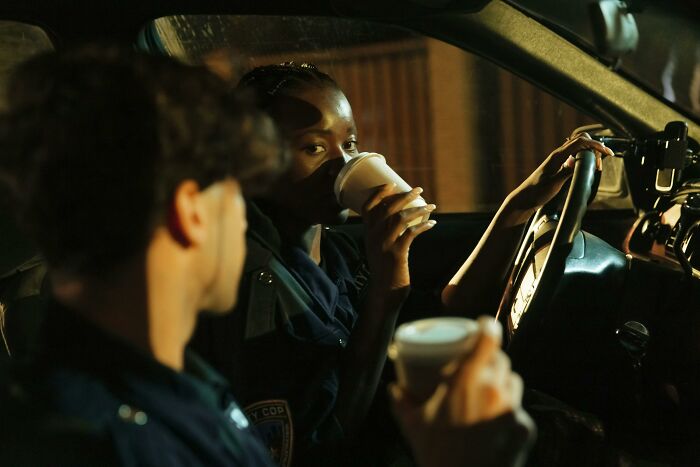 Two women police officers sitting in a car, sipping coffee during a night shift, showcasing the WomenInMaleFields trend.