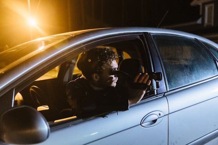 Man in a car at night, filming with a camcorder, representing jobs that seem fun but might not be as enjoyable as imagined.