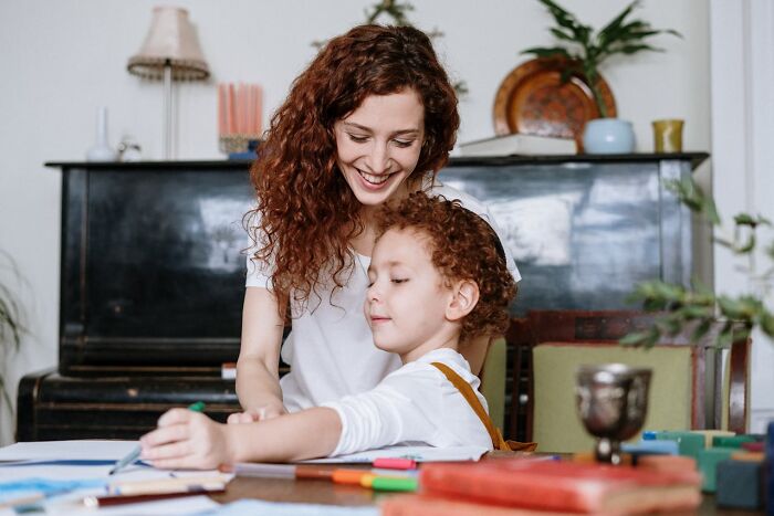 Woman smiling while helping child with homework, showcasing job secrets in a cozy setting.