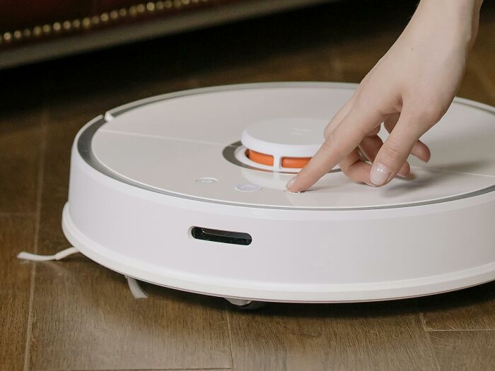 A person using a frugal home hack with a robot vacuum to clean hardwood floors.