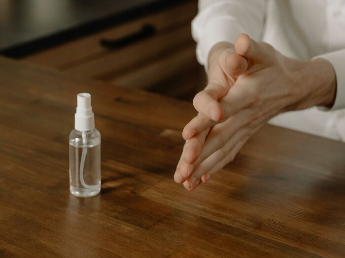 Hands sanitizing with peace and quiet, a small spray bottle rests on a wooden table.