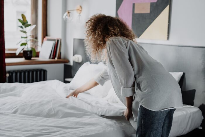 Person with curly hair making a bed, emphasizing good hygiene habits.