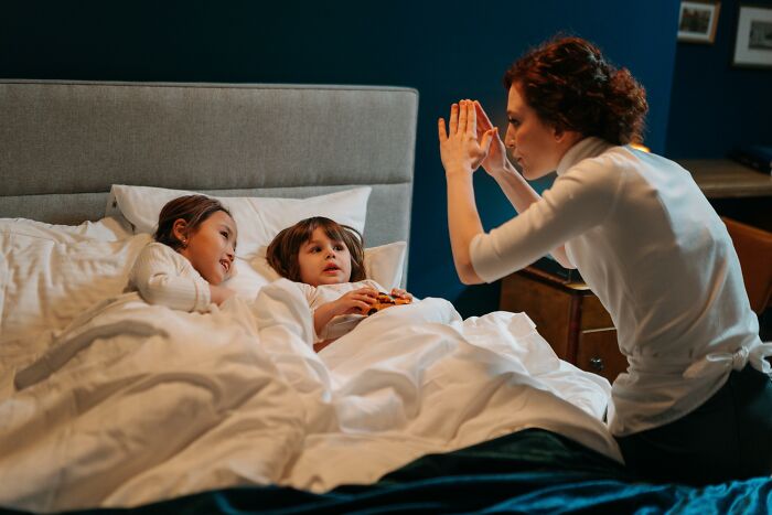 A woman making shadow puppets for two children in bed, creating a cozy and imaginative atmosphere.