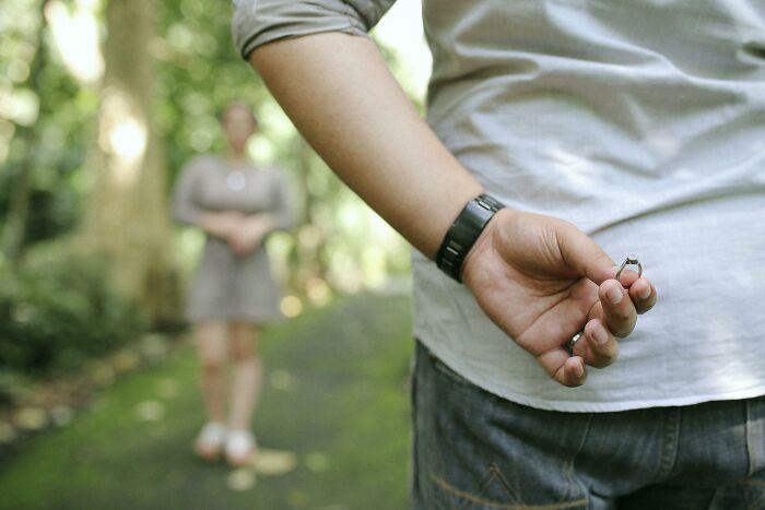 Person holding a ring behind their back, about to reveal a secret proposal.