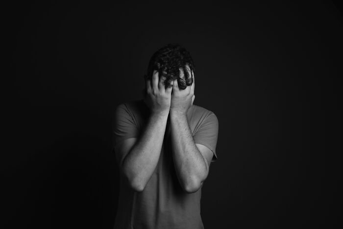 Person in distress with hands on face, symbolizing survival against odds in a dark setting.