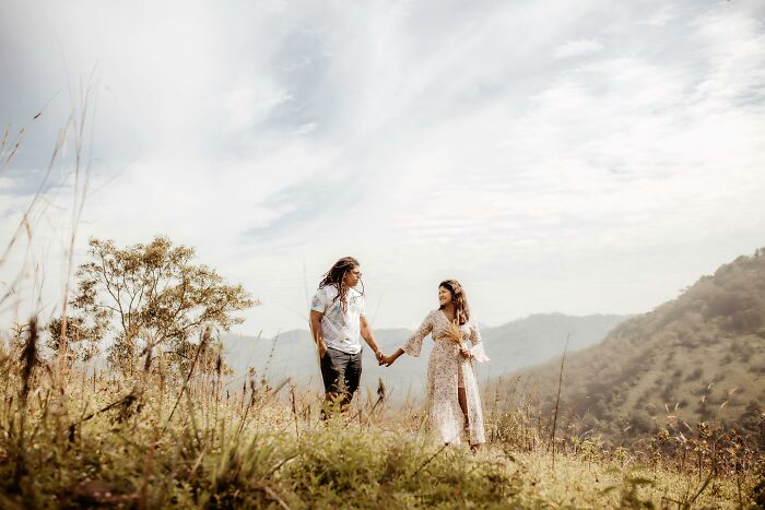 Couple holding hands on a grassy hill under a cloudy sky, embodying people sharing secrets in nature.