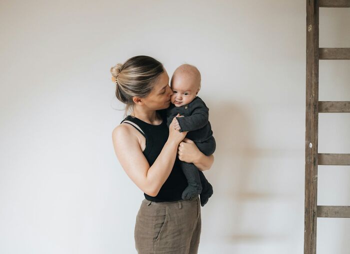 Woman holding a baby, kissing its cheek, in a minimalistic room.