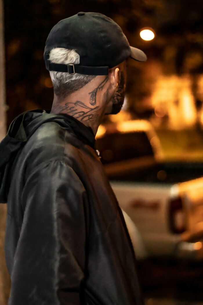 Person with neck tattoos wearing a cap and jacket at night, illustrating professions as potential dealbreakers.