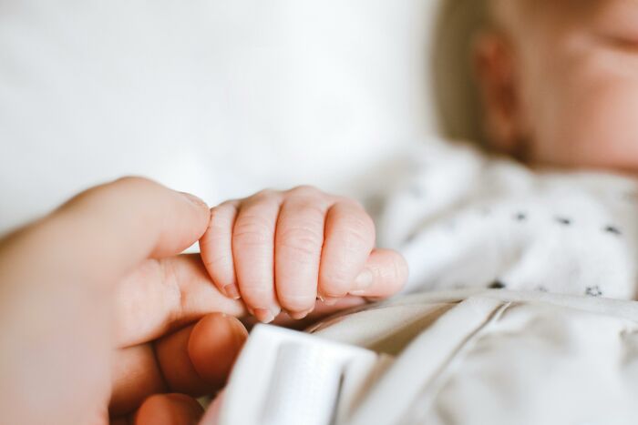 Baby holding an adult's finger, symbolizing survival against all odds, in a tender moment of connection and resilience.