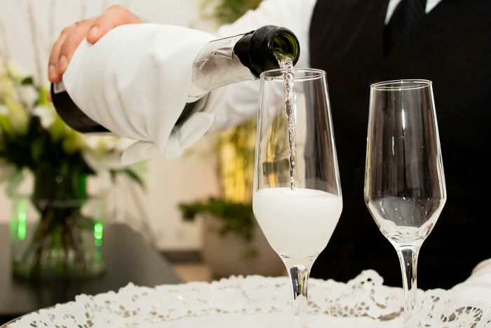 Pouring champagne into a glass at a festive event, highlighting social gatherings where people may share secrets.