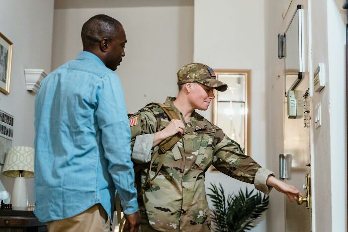 Woman in military uniform with a man, part of the WomenInMaleFields trend, entering a room.