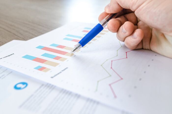 Close-up of a hand with a pen analyzing job insights on a printed graph chart.