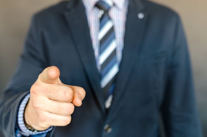 Person in a suit pointing directly at the camera, focusing on the concept of people getting fired.