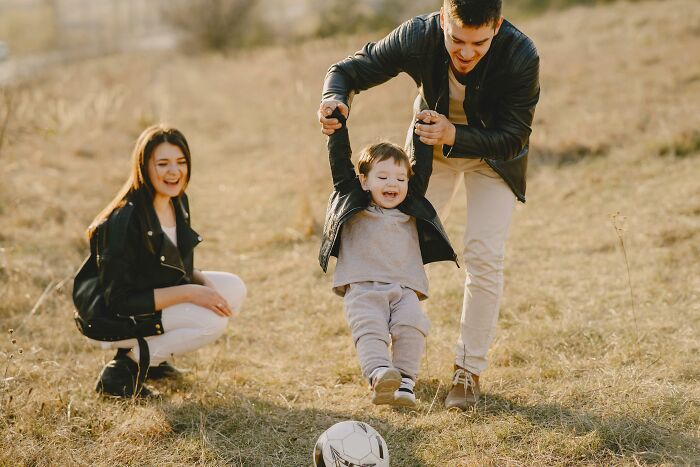 A family enjoying time outdoors with a child swinging happily and a soccer ball nearby.